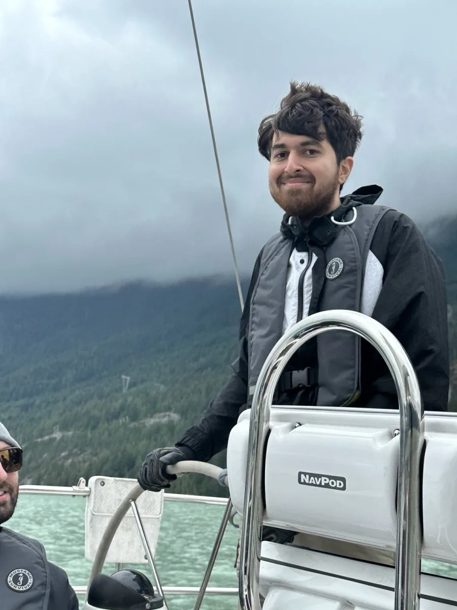 Payam at the helm of a sailboat in Squamish, with misty mountains behind him.